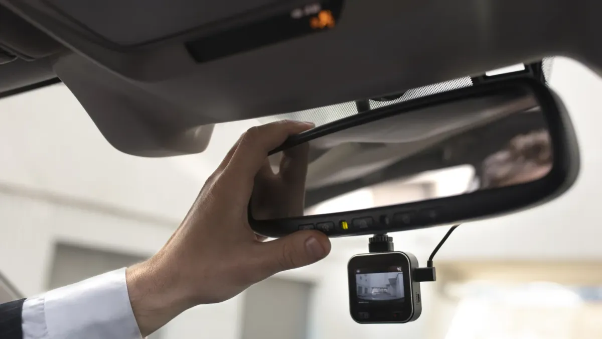Řidič upravuje zpětné zrcátko, pod kterým je připevněná autokamera