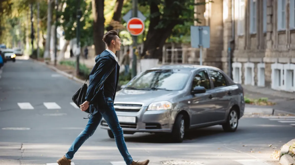 Muž přechází po přechodu pro chodce, za ním stojí osobní auto
