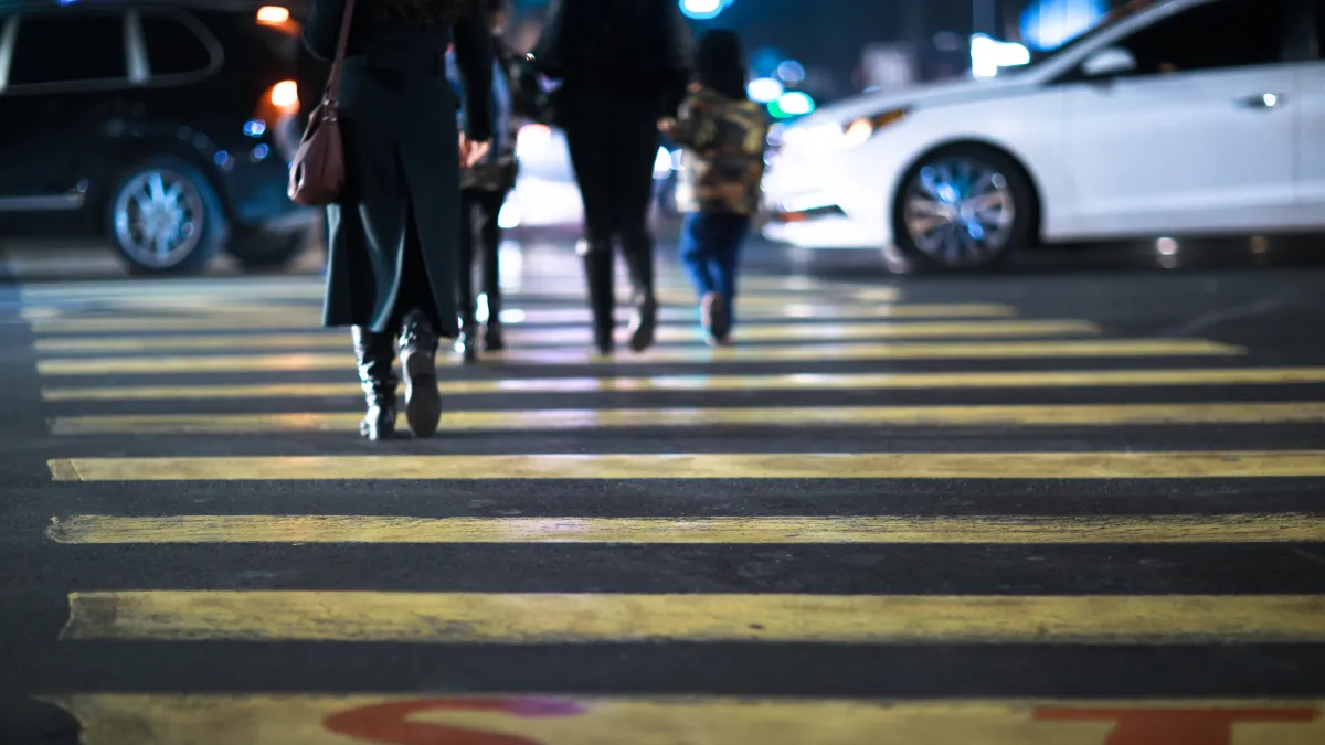 Chodci na přechodu ve večerním městě, vedle projíždí auto
