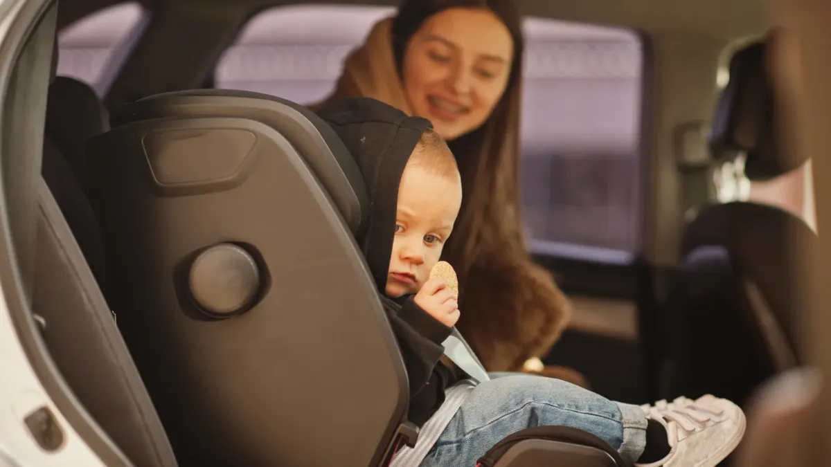 Matka připoutává malé dítě v autosedačce