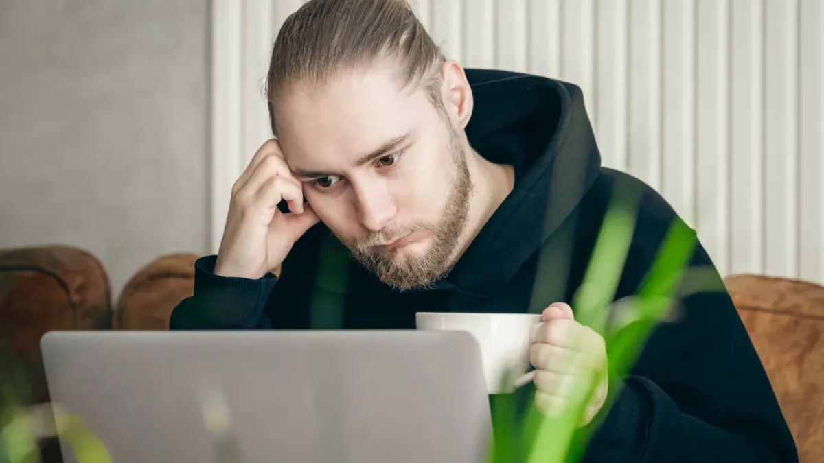 Frustrovaný mladý muž sedí u notebooku a drží se za hlavu