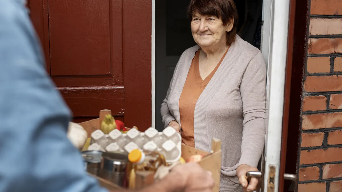Starší žena u dveří přebírá nákup od sousedky