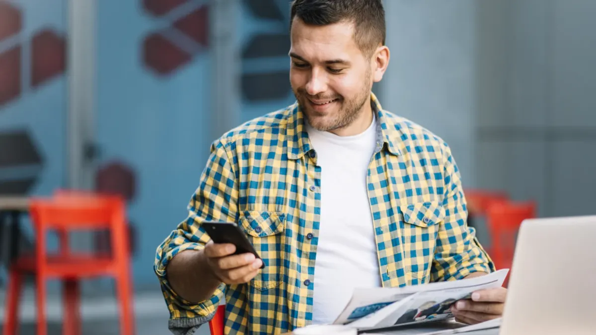 Muž v kavárně s notebookem používá mobil