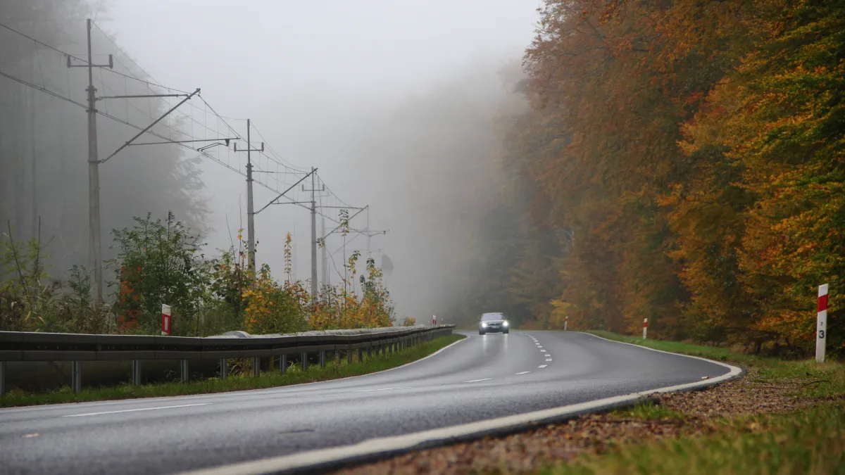 Auto projíždí mlhavou podzimní silnicí lesem
