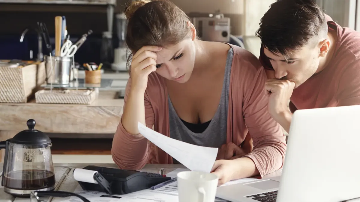 Mladý pár ustaraně čte dokumenty u notebooku v kuchyni