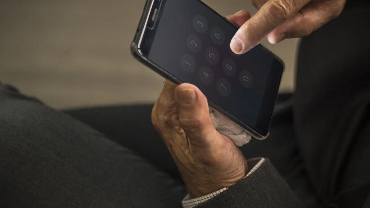 Muž v obleku zadává kód do mobilního telefonu
