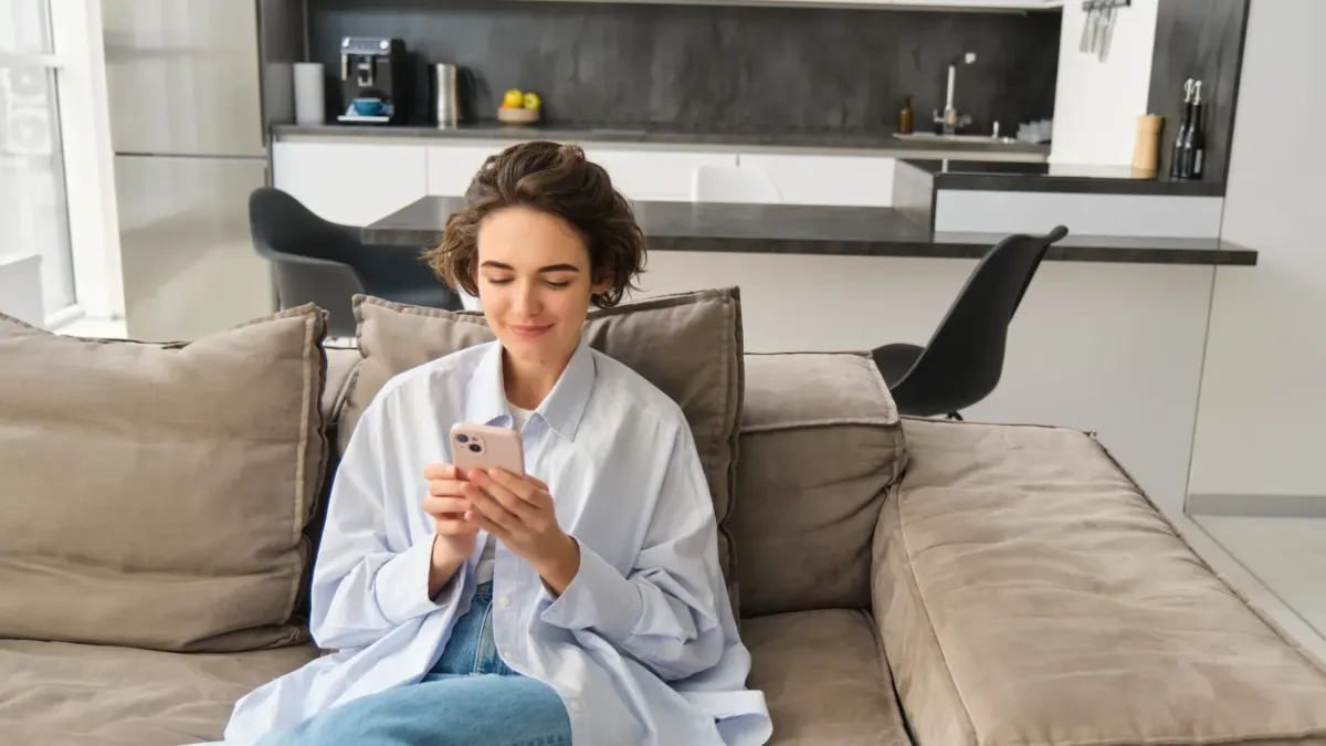 Žena sedí na pohovce a prohlíží si chytrý telefon