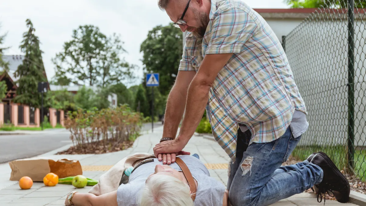 Muž provádí masáž srdce starší ženě na ulici